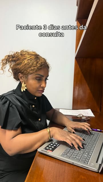 Andréa Maia sentada à mesa, analisando a ficha de uma paciente no notebook.